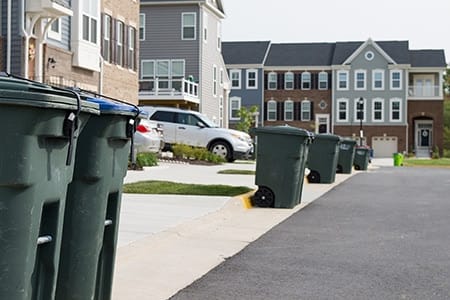trash and recycling cans with strong straps line the street in a townhome complex